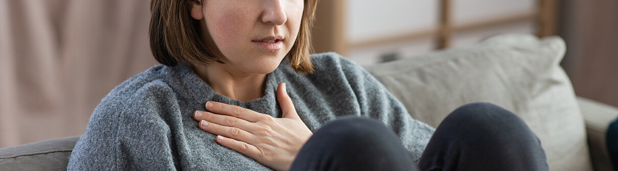 Photo of a woman sitting on her couch holding her hand to her chest. Are you struggling with your anxiety symptoms? Learn how anxiety therapy in Atlanta, GA can help you overcome your anxiety symptoms.