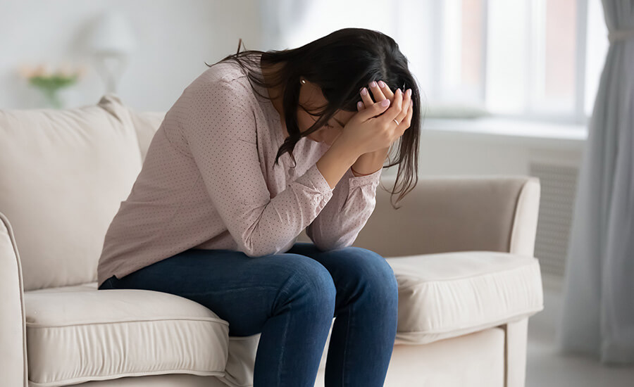 Photo of a woman sitting on a couch with her head in her hands. This photo represents how overwhelming grief can be and how grief counseling in Atlanta, GA can help you ease your symptoms.