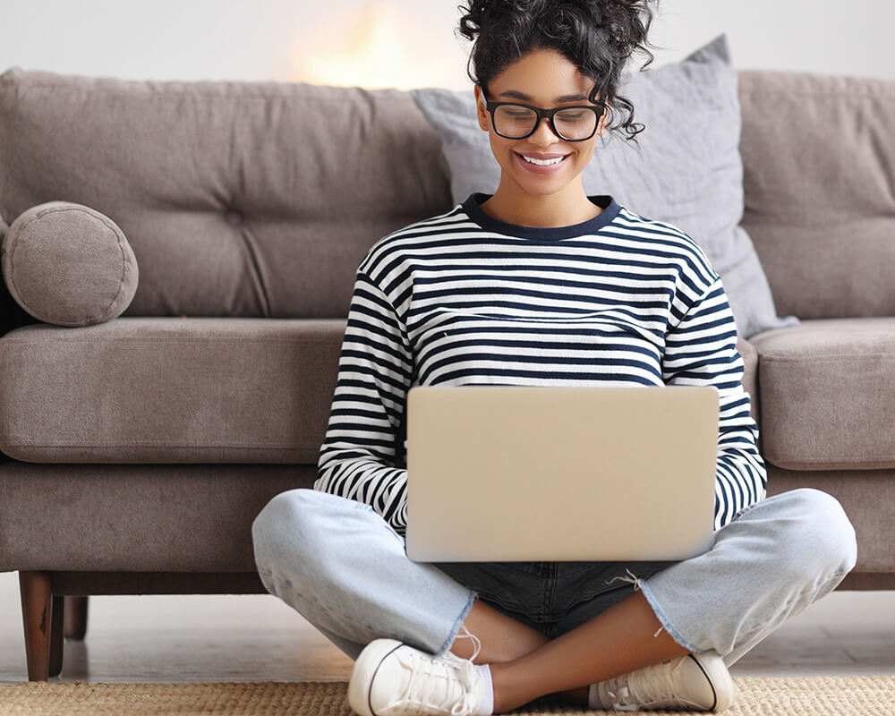 Photo of a woman sitting on the floor holding her laptop and smiling. Learn how an anxiety therapist in Atlanta, GA can help you overcome your anxiety symptoms.