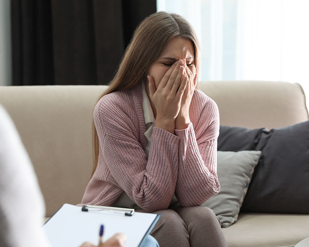 Photo of a woman sitting on a couch with her hands covering her mouth looking upset. This photo represents how your depression can feel like it’s controlling your life. Learn how depression therapy in Atlanta, GA can help you overcome your symptoms.