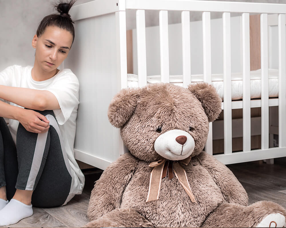 Image of a woman sitting on the nursery floor looking sad. Learn to manage your postpartum emotions with the help of postpartum therapy in Atlanta, GA.