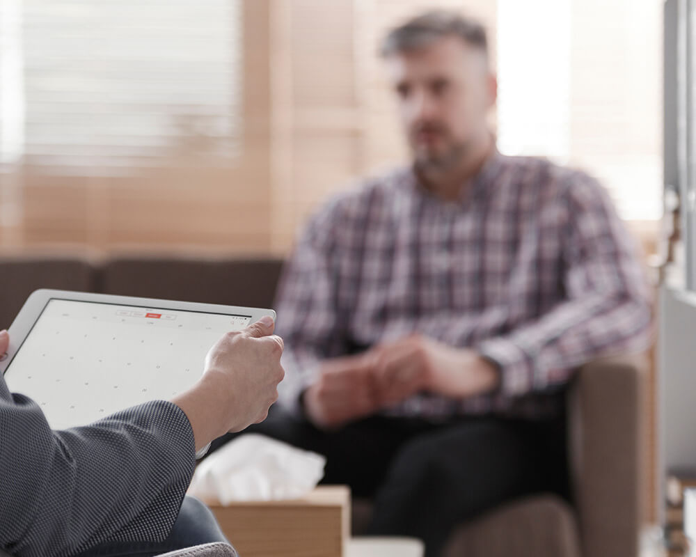 Blurry photo of a man sitting on a couch speaking with a grief therapist in Atlanta, GA. Learn how grief counseling in Atlanta, GA can help you overcome your grief symptoms.