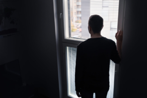 Photo of a sad man standing beside a window looking out. Discover how grief counseling in Atlanta, GA can help you process your grief and begin to overcome your grief symptoms.