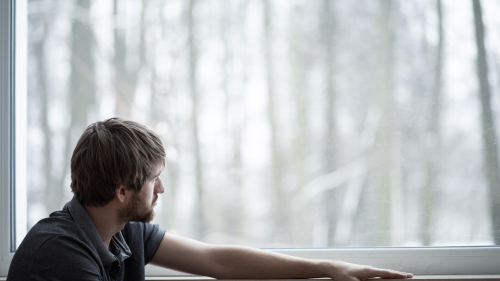Photo of a depressed man looking out a window. This photo represents how without depression therapy in Atlanta, GA you may continue to struggle with your depression symptoms.