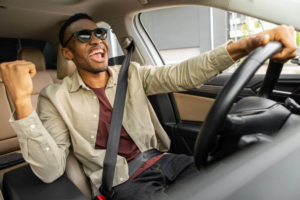Photo of an African American man driving in his car smiling and holding up his fist in victory representing how therapy for stress management in Atlanta, GA can help you overcome your stress symptoms and live a stress free life.