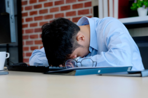 Photo of an Asian American man laying his head down on a table looking stressed. This photo represents how overwhelming stress triggers can be. Learn how to identify you stress triggers and begin to cope with therapy for stress management in Atlanta, GA.