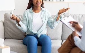 Photo of a woman happily sitting on a couch speaking with a therapist. This photo represents how depression therapy in Atlanta, GA can help provide you support ot help you better manage your symptoms and live a happier life.