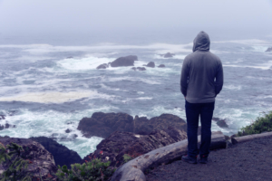Photo of a man standing by the ocean on a stormy day. This photo represents how depression can seem overwhelming and make you feel isolated. With depression therapy in Atlanta, GA you can begin to overcome your depression symptoms in a supportive space.
