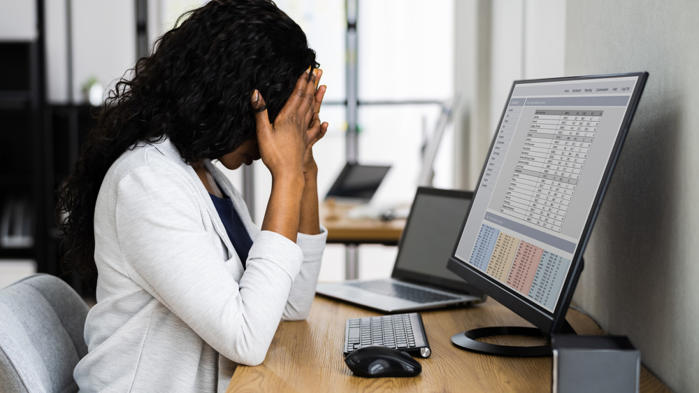 Photo of an African American woman sitting at a desk with her hands on her head showing stress. This photo represents how stress can become overwhelming and how therapy for stress management in Atlanta, GA can help you start to manage your symptoms.