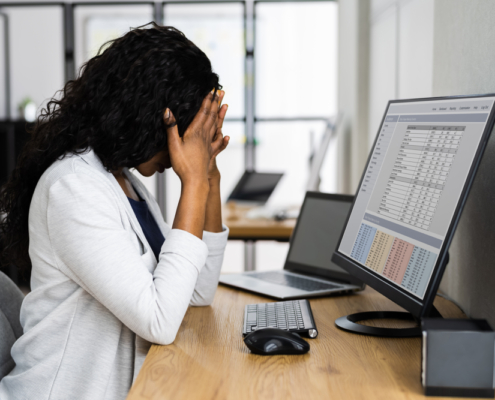 Photo of an African American woman sitting at a desk with her hands on her head showing stress. This photo represents how stress can become overwhelming and how therapy for stress management in Atlanta, GA can help you start to manage your symptoms.