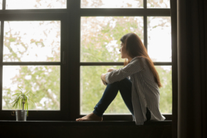 Photo of a woman sitting on a window ledge holding her knees and looking outside. Looking to find ways to manage your anxiety? Learn how a skilled anxiety therapist can help you overcome your symptoms. With anxiety therapy in Atlanta, GA you can begin healing.