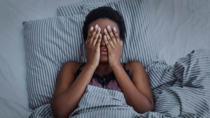 Photo of an African American woman laying in bed covering her eyes with her hands. Struggling to manage your stress symptoms and it's keeping you from sleeping? With therapy for stress in Atlanta, GA you can begin learning new ways to manage your stress in an effective way.