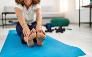 Photo of a woman sitting on a yoga mat smiling and stretching. If you're looking for ways to begin managing your day-to-day stress, learn here the techniques you can begin using. Start therapy for stress in Atlanta, GA for more support.