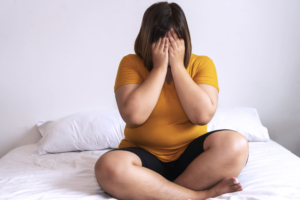 Photo of an upset woman sitting on a bed covering her face. Stress can be unbearable when unmanaged. Learn effective stress reducing techniques here and seek more support with therapy for stress in Atlanta, GA. 