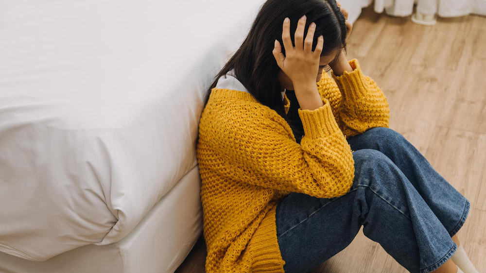 Photo of a young woman sitting on the floor holding her head. Are you struggling with your depression symptoms? Find support with depression therapy in Atlanta, GA.