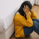 Photo of a young woman sitting on the floor holding her head. Are you struggling with your depression symptoms? Find support with depression therapy in Atlanta, GA.