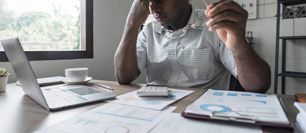 Photo of a stressed man pinching his nose while working. Struggling to overcome your depression symptoms at work? Learn tips from a depression therapist in Atlanta, GA on managing your symptoms to work more effectively.