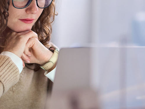 Photo of a woman resting her head on her hands and looking at a laptop. Discover ways to be productive at work when dealing with your depression from a depression therapist in Atlanta, GA.