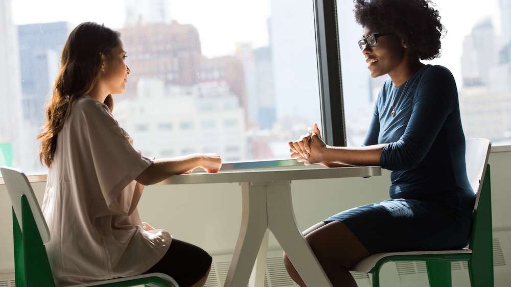 Photo of two women sitting at table talking. Wondering if seeking depression therapy in Atlanta, GA is right for you? Learn how to effectively work through your symptoms.