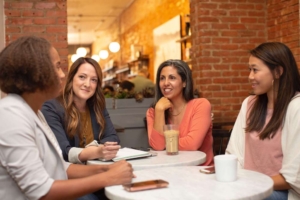 Photo of a group of happy friends sitting at a table and talking. Learn to develop healthy coping strategies to manage your anxiety triggers with the help of an anxiety therapist during anxiety therapy in Atlanta, GA.