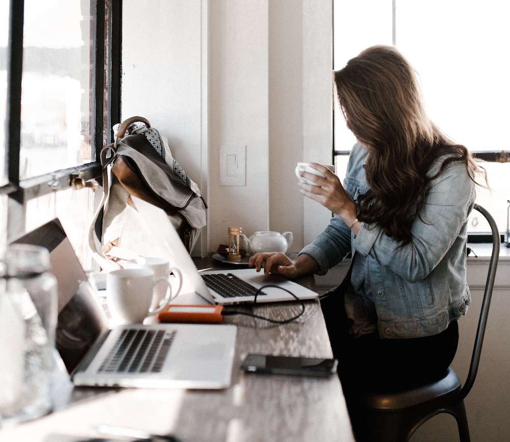 Photo of a woman drinking out of a mug and working on a laptop. Begin coping with your work depression and improve your work performance with the help of a depression therapist in depression therapy in Atlanta, GA.