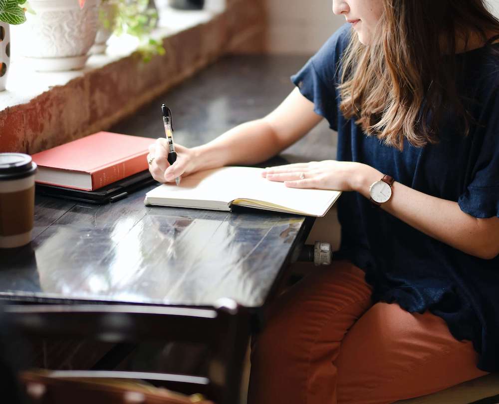 Photo of a woman sitting at a desk writing in a journal. Learn different ways you can manage your anxious thoughts with the help of anxiety therapy in Atlanta, GA.
