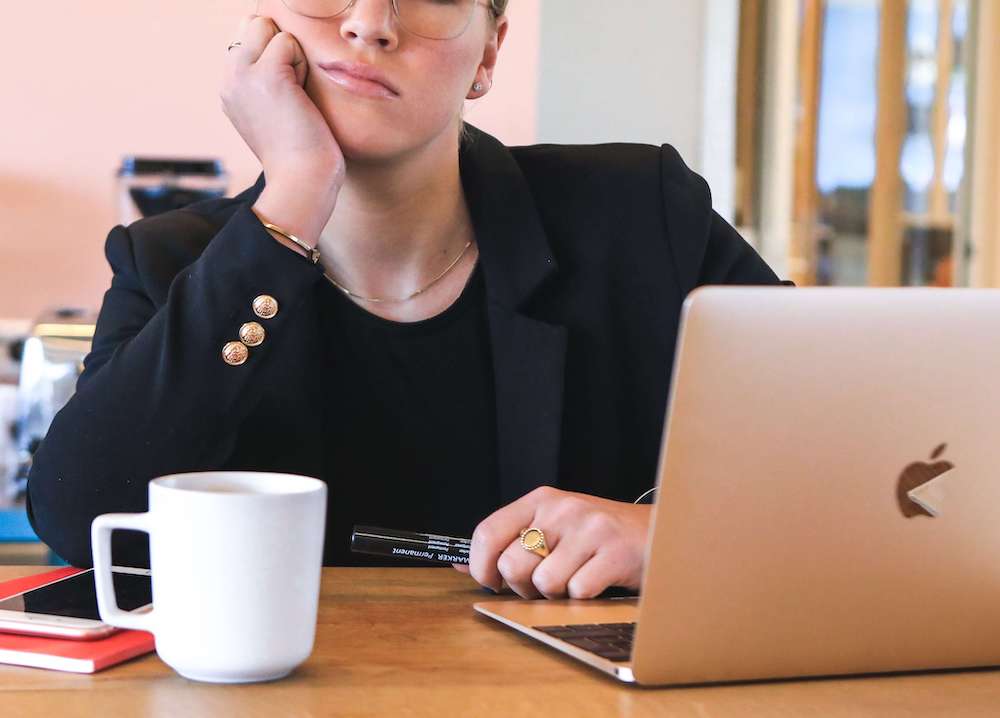 Image of a professional business woman sitting at a desk with a mug and laptop holding her hand to her chin. Identify your source of sadness when you're working. Learn how depression therapy in Atlanta, GA can help you cope!