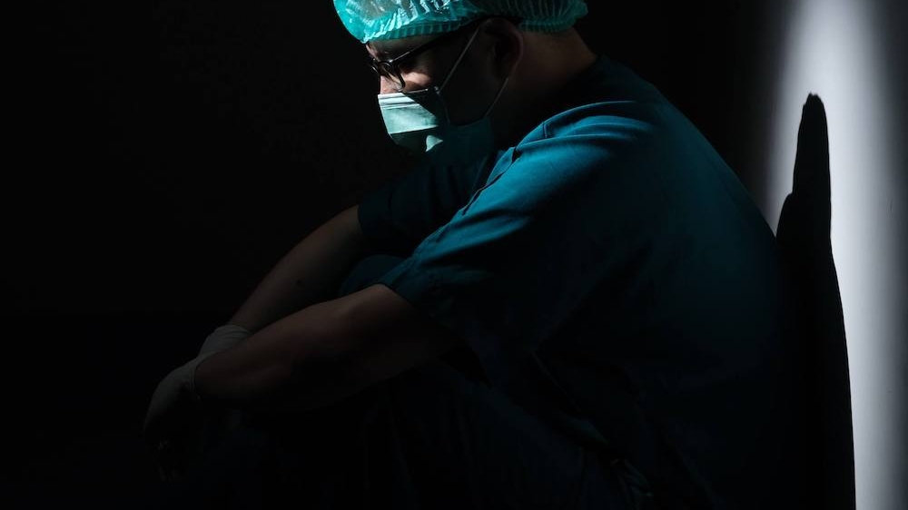 Image of a medical professional sitting on the floor in the dark. Overcome your depression so you can refocus on your work with the help of depression therapy in Atlanta, GA.