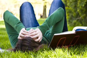 A college student lays on their back in the grass next to an open textbook while covering their face. This could represent how academic anxiety can affect individuals. Learn more about anxiety therapy in Atlanta, GA and how an online anxiety therapist in Atlanta, GA can offer support today. 