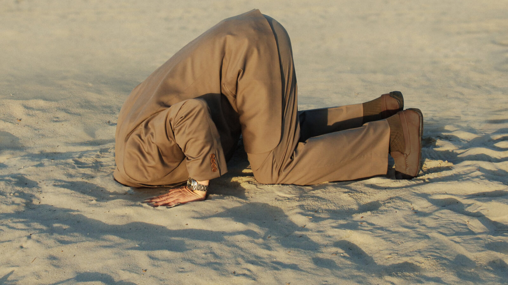A man in a business suit buries their head in the sand, representing an avoidance behavior. Learn how an online anxiety therapist in Atlanta, GA can offer support with stress and anxiety counseling in Atlanta, GA. Search for anxiety therapy in Atlanta, GA and how an anxiety therapist in Atlanta, GA can help today.