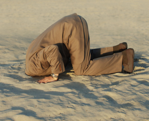 A man in a business suit buries their head in the sand, representing an avoidance behavior. Learn how an online anxiety therapist in Atlanta, GA can offer support with stress and anxiety counseling in Atlanta, GA. Search for anxiety therapy in Atlanta, GA and how an anxiety therapist in Atlanta, GA can help today.