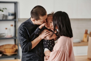 Photo of happy parents kissing their baby. Through postpartum anxiety treatment in Atlanta, GA, you can begin to feel like yourself again while nurturing your relationship with your partner. Meet with a postpartum therapist in Georgia for the support you need.