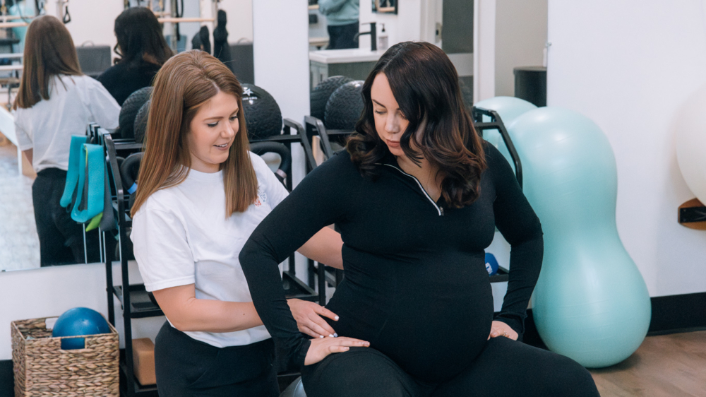 A postpartum therapist in Atlanta, GA helps a pregnant woman with gentle core exercises on a stability ball, supporting her through postpartum therapy in Atlanta, GA and offering care that complements postpartum anxiety treatment in Atlanta.