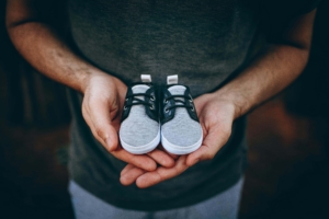 A hopeful father holds tiny gray baby shoes with care, reflecting the emotional journey of pregnancy therapy in Atlanta, GA and the supportive role of grief & loss therapy in Atlanta during pregnancy after loss and alpharetta postpartum anxiety treatment. 