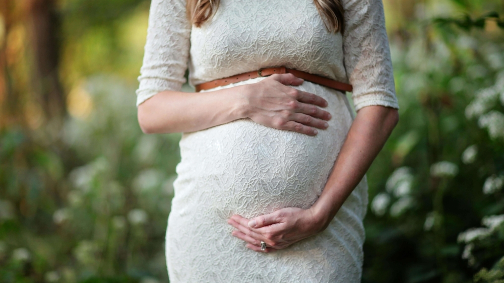 Close-up of a pregnant woman in a white lace dress gently holding her stomach in a serene outdoor setting, symbolizing pregnancy therapy in Atlanta, GA, and the compassionate care of a perinatal therapist in Atlanta, GA for those navigating grief & loss therapy in Atlanta.