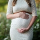 Close-up of a pregnant woman in a white lace dress gently holding her stomach in a serene outdoor setting, symbolizing pregnancy therapy in Atlanta, GA, and the compassionate care of a perinatal therapist in Atlanta, GA for those navigating grief & loss therapy in Atlanta.
