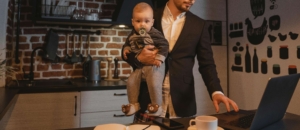 A father balances work and parenting while holding his baby and managing tasks on a laptop—highlighting the need for ADHD treatment in Atlanta, GA and support from an ADHD therapist in Atlanta, GA through ADHD therapy Atlanta, GA. 