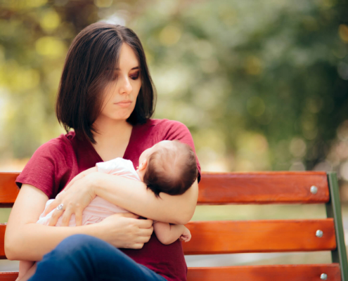 A new mother sits on a park bench holding her baby, appearing overwhelmed—symbolizing the emotional weight that postpartum therapy in Atlanta, GA or postpartum anxiety treatment in Atlanta can help address.