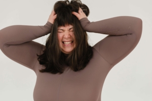 A woman clutches her hair in frustration, eyes closed, and face tense with emotion — a raw depiction of postpartum rage in Atlanta, GA. This powerful image highlights how emotional dysregulation can show up after giving birth. If you're feeling this way, you're not alone. A postpartum therapist in Alpharetta can support you with personalized care, and Alpharetta postpartum anxiety treatment can offer tools for emotional regulation. 