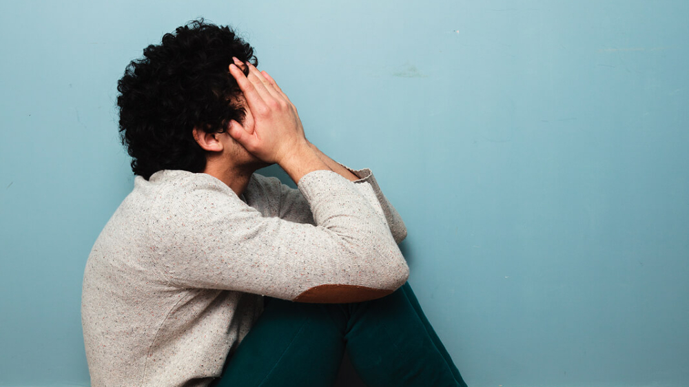 A distressed man sits on the floor covering his face, symbolizing emotional pain and overwhelm. A trauma therapist in Atlanta, GA can provide support through trauma therapy in Atlanta, GA and help address related struggles often seen in depression therapy in Atlanta, GA.
