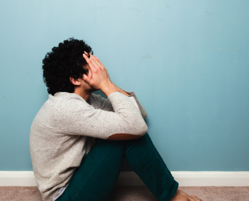 A distressed man sits on the floor covering his face, symbolizing emotional pain and overwhelm. A trauma therapist in Atlanta, GA can provide support through trauma therapy in Atlanta, GA and help address related struggles often seen in depression therapy in Atlanta, GA.