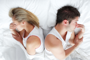 A couple lies in bed facing away from each other, both appearing disconnected and emotionally distant. This scene represents the strain postpartum struggles can place on relationships. Postpartum therapy in Atlanta, GA helps couples navigate the emotional challenges that come with new parenthood. A postpartum therapist in Alpharetta can offer tools for communication and healing during this vulnerable season. 