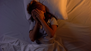 Woman in bed covering her face at night, illustrating sleeplessness and worry. Begin online anxiety therapy in Atlanta, GA, connect with an anxiety therapist in Atlanta, GA, and explore personalized therapy for anxiety in Atlanta, GA. 