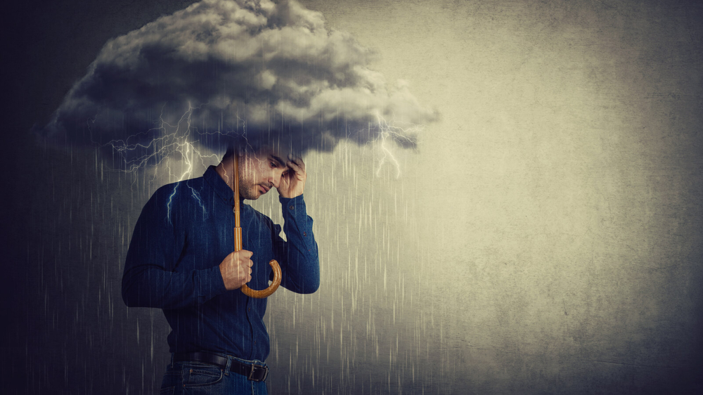 A man stands under a storm cloud, holding an umbrella as rain pours—capturing the heaviness of loss and worry. Support like grief counseling in atlanta, ga with a compassionate grief therapist in atlanta, ga can also include therapy for anxiety in atlanta, ga to ease the pressure.