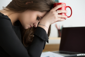 stressed woman holding cup | grief therapist in atlanta, ga | online grief counseling in atlanta, ga | anxiety therapy in atlanta, ga | atlanta, ga Stressed woman rests her forehead on a red mug beside her laptop, feeling overwhelmed at work and home. Discreet online grief counseling in atlanta, ga, guided by a trusted grief counselor in atlanta, ga, can be paired with anxiety therapy in atlanta, ga for steadier days.